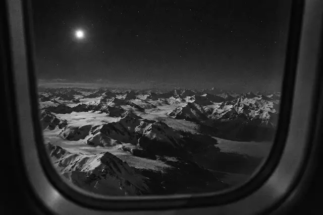 Illustration: snow-covered Alaskan mountains at night, seen through an airliner window. AI-generated scene of the location, not evidence.